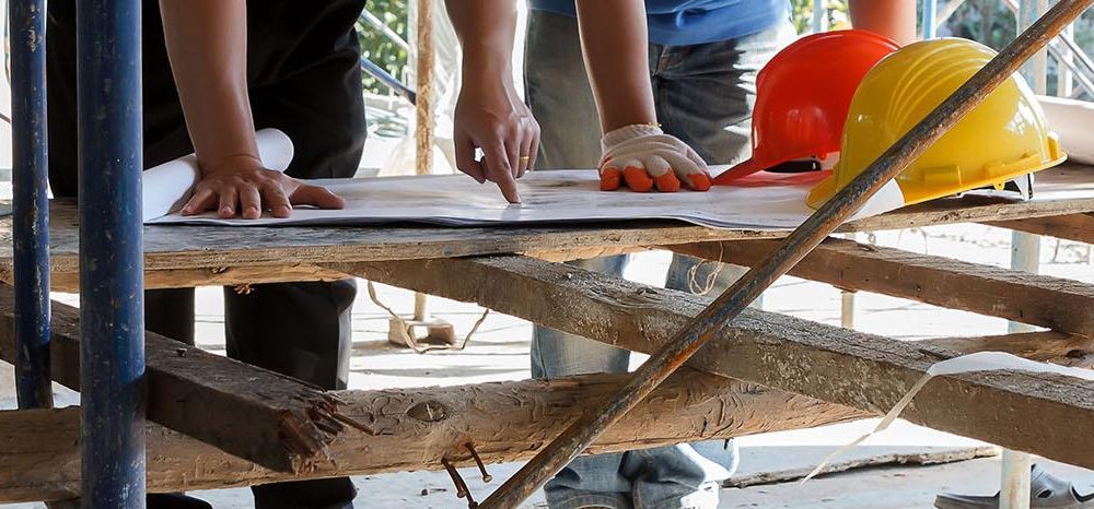Two construction workers examinining blueprints on a wooden table at a construction site