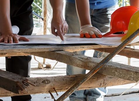 Two construction workers examinining blueprints on a wooden table at a construction site